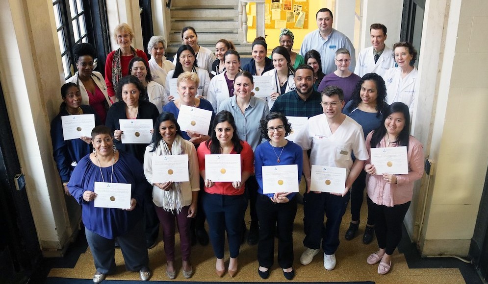Members of Columbia Health standing by stairs, holding their certificates of accreditation by the Accreditation Association for Ambulatory Health Care (AAAHC).
