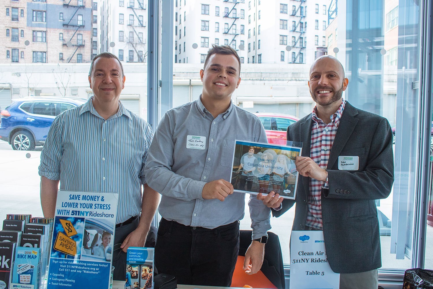 Three men standing in front of a Clean Air NY table with lots of pamplets on it, with one giving a Clean Air NY certificate to Daniel Allalemdjian, director of transportation management at Environmental Stewardship