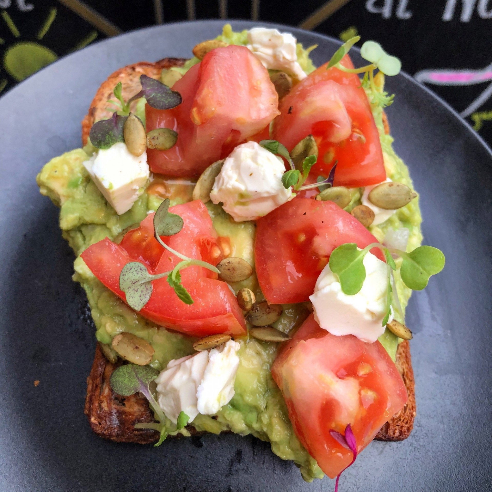 Avocado toast with goat cheese, pumpkin seeds, and tomatoes on a blue plate