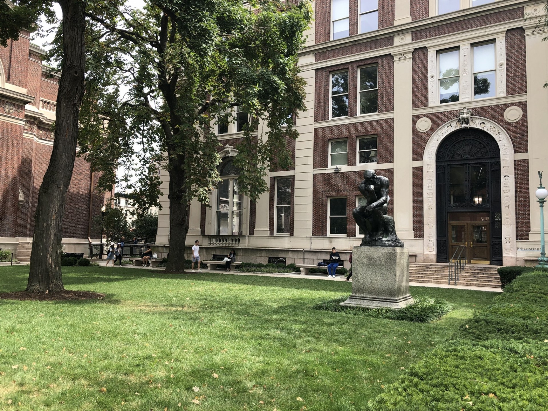 Philosophy lawn, with trees and The Thinker statue, with students sitting on three concrete benches along Philosophy Hall.