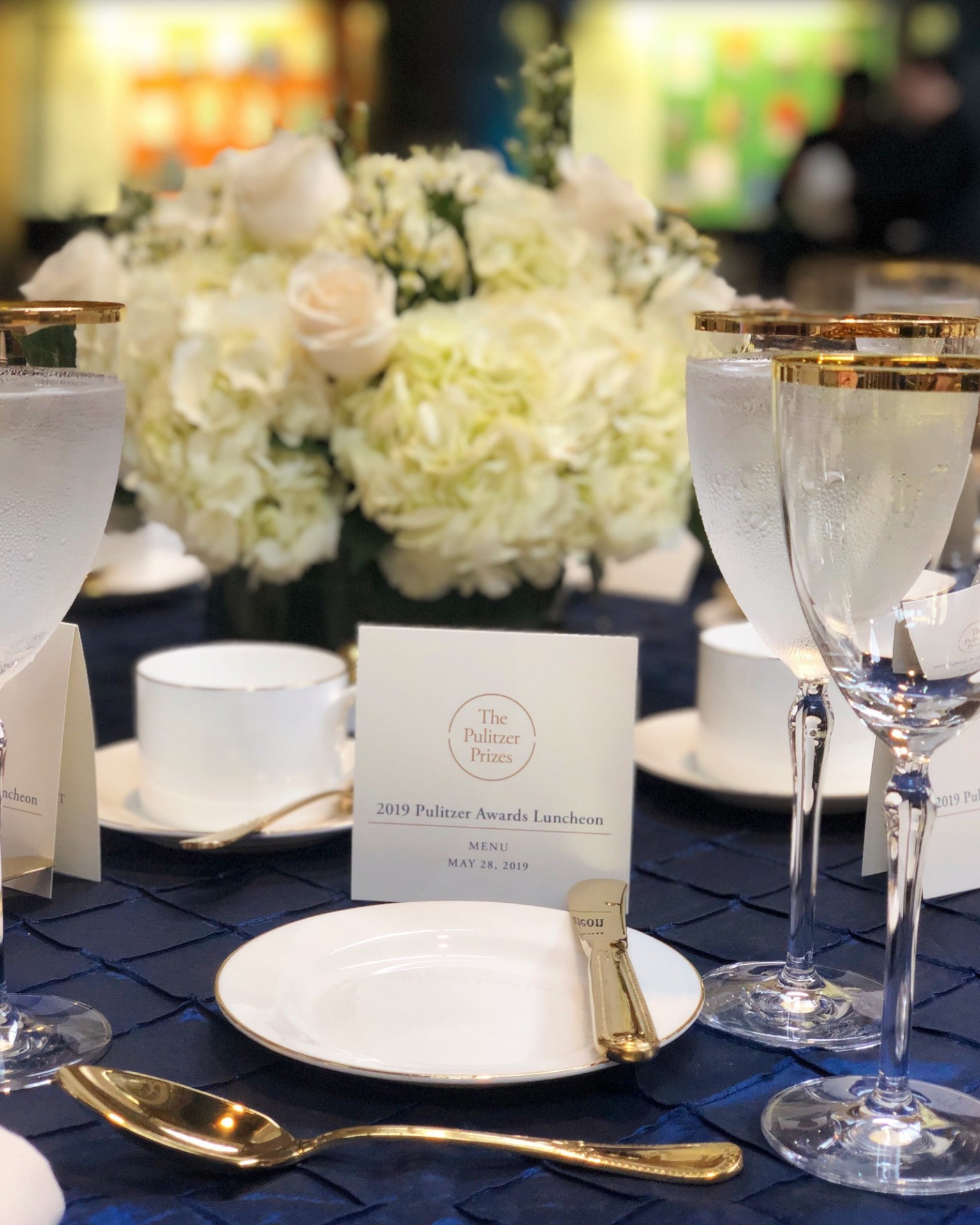 A table with white flowers, a place setting, and a white menu card.