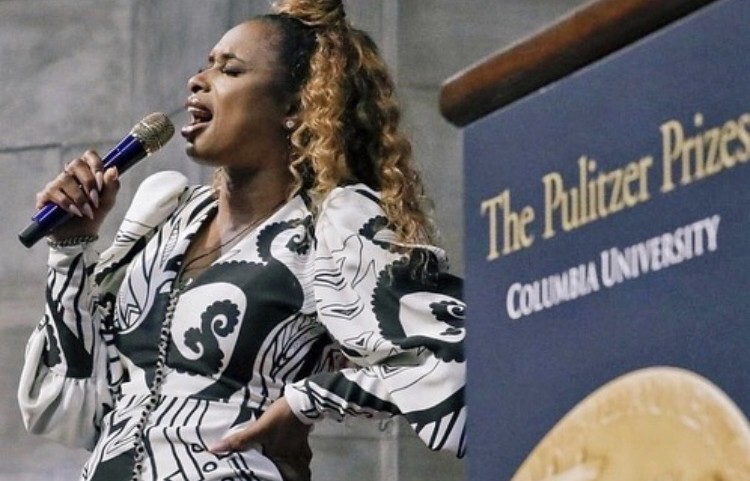 Jennifer Hudson singing into a blue microphone, wearing a white and black top