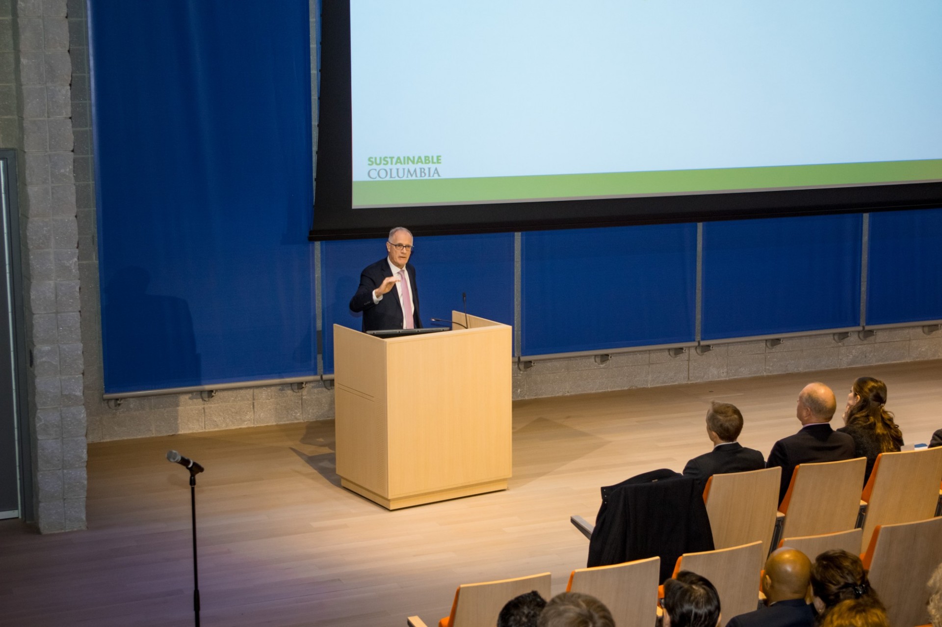 Sir Alex Halliday, director of the Earth Institute, gave a keynote speech during the ceremony. Alex Halliday speaking at a wooden podium, next to a large projection screen and blue wall.