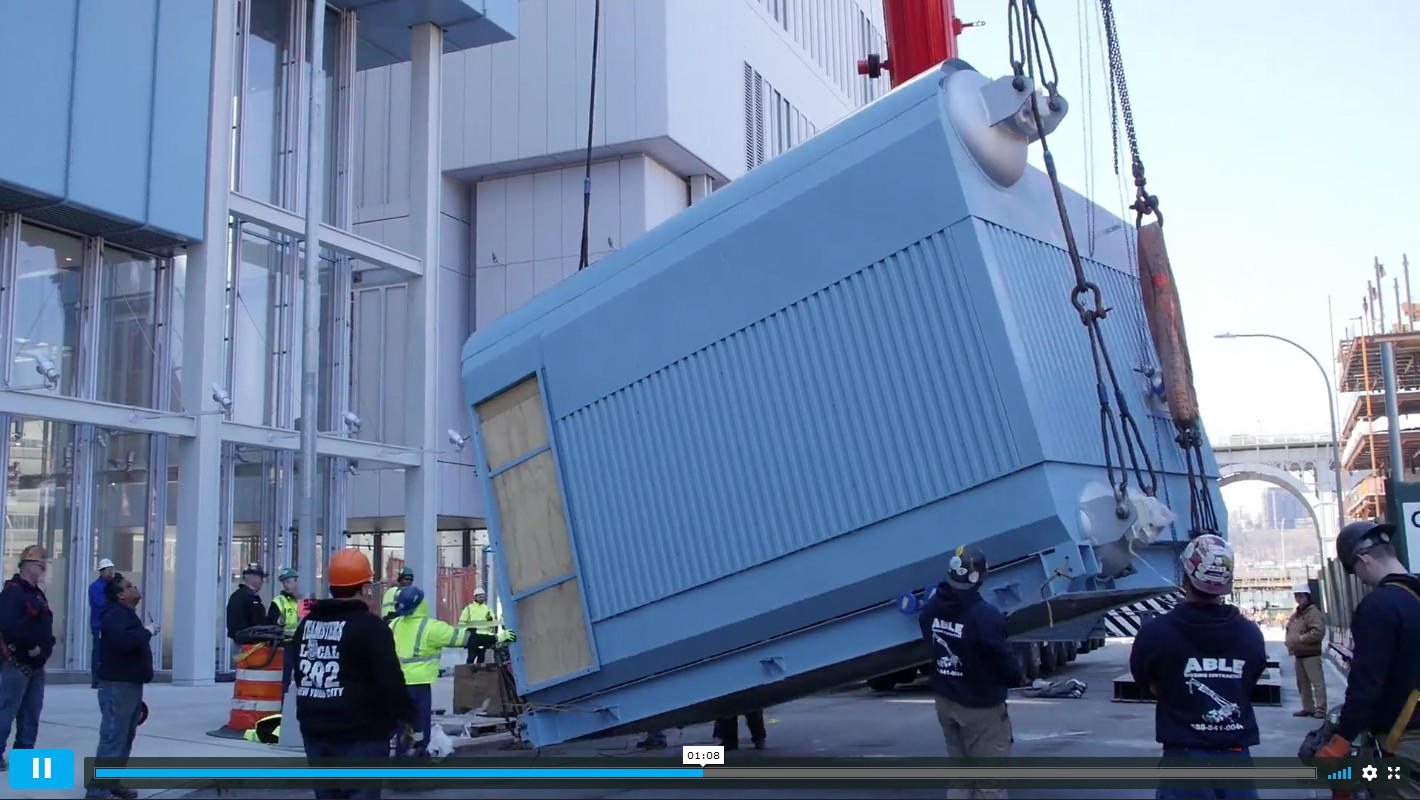 Screenshot of video detailing the Central Energy Plant's boiler installation, showing the equipment being hoisted from the ground, surrounded by workers.