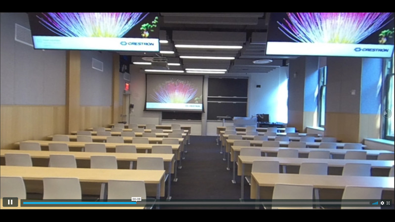 A screenshot of the 360-degree video of the accessible spaces in Chandler Hall, with rows of tables and chairs, two screens overhead, and a projector screen pulled down against the wall.
