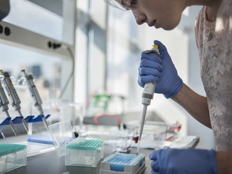 A woman with blue gloves in a lab, using a syringe 