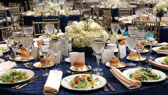 A place setting with food, flowers, on a table with a dark blue table cloth